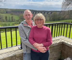 Susan and Graham standing together on a veranda in front of a viaduct